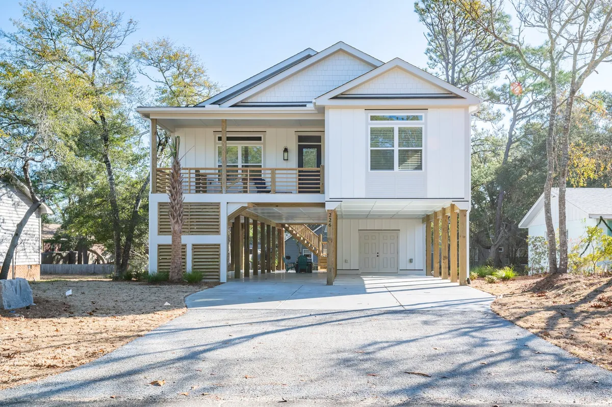 This image features the house structure prominently, with a wide driveway, porch, and an inviting, sunlit yard bordered by trees. The driveway's ample space hints at generous parking for multiple vehicles, aligning with the section's emphasis on flexibility for travelers with cars or boat trailers. The welcoming exterior also signals modern comfort and accessibility.