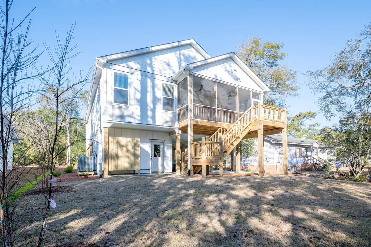 A welcoming screened porch and deck area attached to a modern home. The space is framed by stairs leading up to the porch, with sunlight filtering in, suggesting a comfortable outdoor spot for socializing or relaxing, especially at sunset.