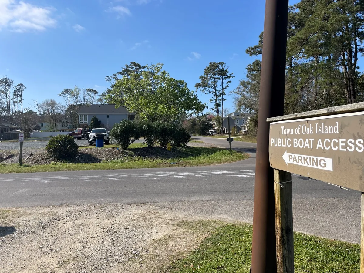 This exterior scene shows a public boat access sign, a large parking area, and a backdrop of trees and nearby homes. The image connects to the nearby attractions and the potential for boating or outdoor adventures, emphasizing both the flexibility and value of the home's location. The spacious parking lot also subtly reinforces the ability to accommodate vehicles or trailers.