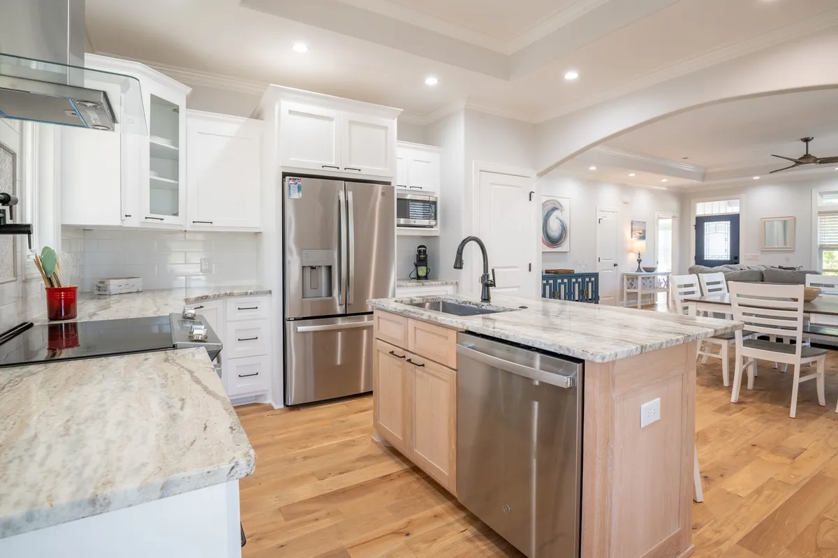 An expansive, modern kitchen with a large island countertop, stainless steel appliances, and white cabinetry, seamlessly connected to an open living area. The space is bathed in natural light, inviting families to cook, dine, and socialize together.
