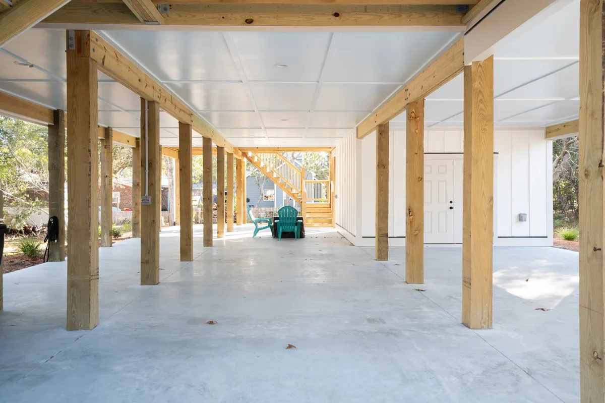 The shaded area beneath the home featuring sturdy wooden support beams, blue chairs for lounging, and a staircase leading up to the main living area. The space is casual and inviting, ideal for relaxing after a day outdoors, storing gear, or socializing in the open air.