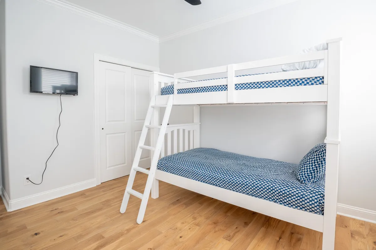 A playful bunk room with built-in bunks, a wall-mounted TV, and wood flooring, creating a fun and cozy atmosphere perfect for children or group stays. The design is practical yet whimsical, with space for both sleep and play.