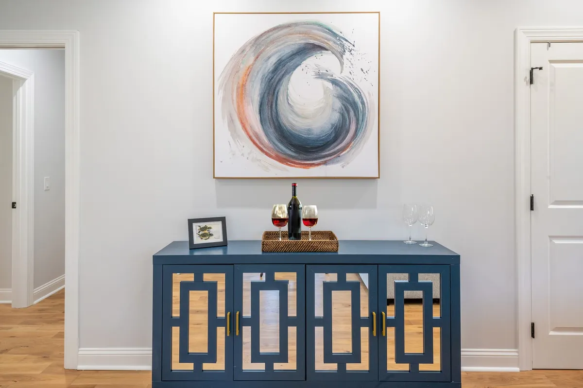 An elegant interior view featuring a blue cabinet, decorative wave artwork, and wine glasses set out, evoking a mood of celebration and sophisticated relaxation. The design conveys an inviting space for hosting or enjoying a quiet drink.